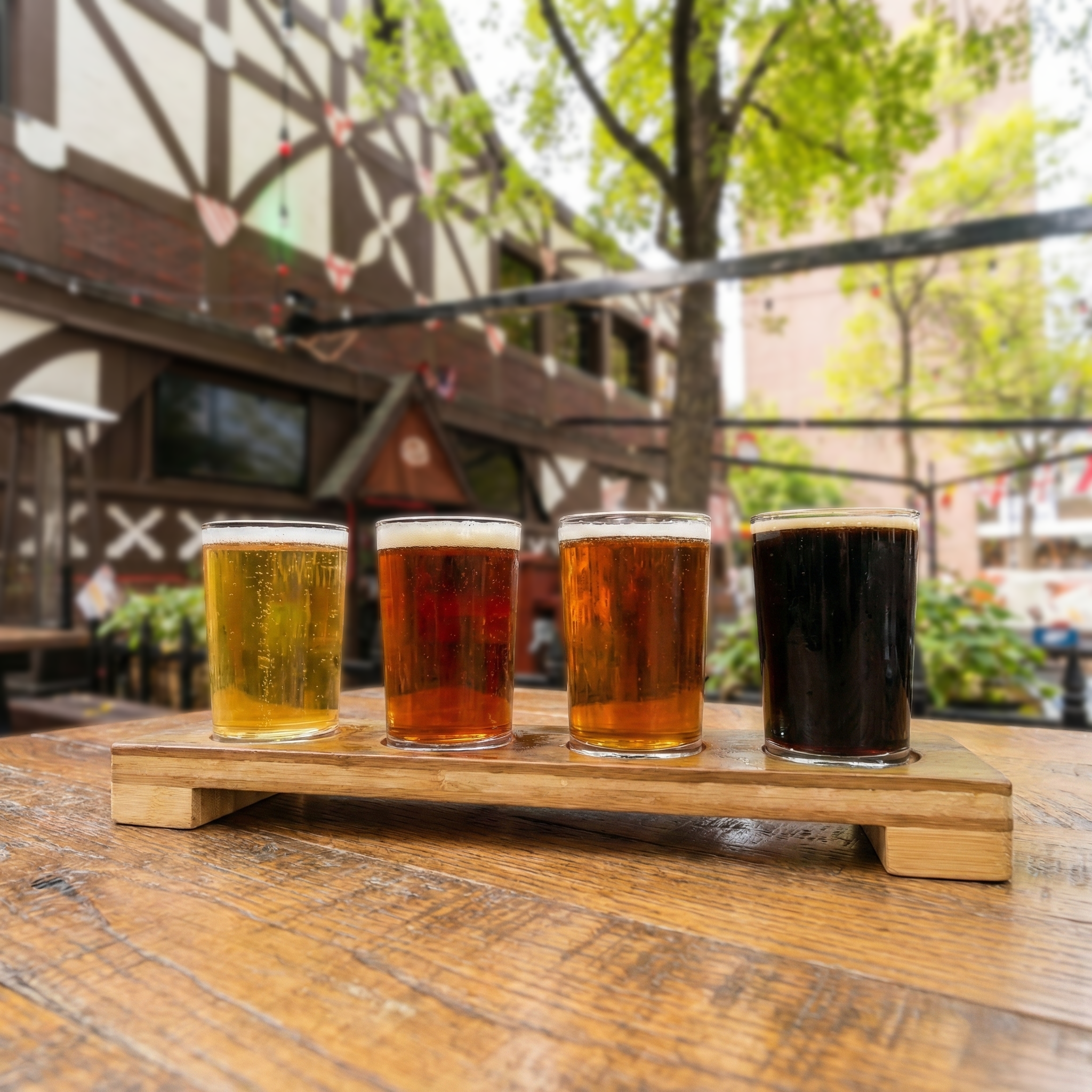Four pints of beer in wooden beer flight on table in outdoor patio in front of German architecture building