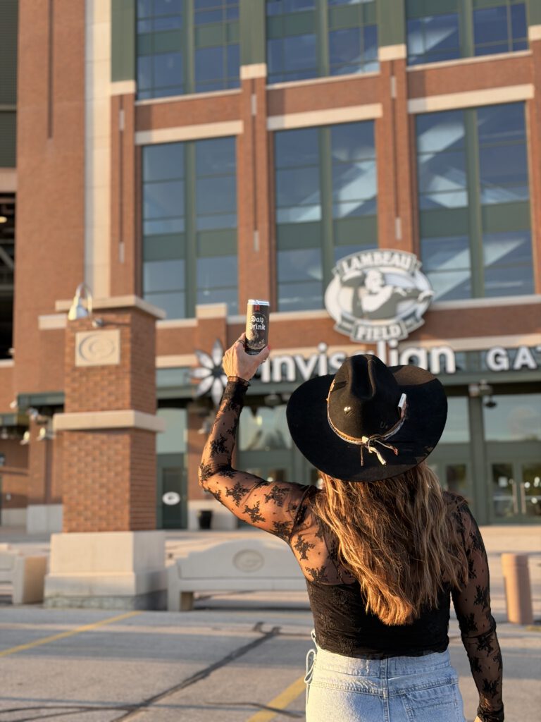 A can of Day Drink held up in the stands at Lambeau Field on a game day.
