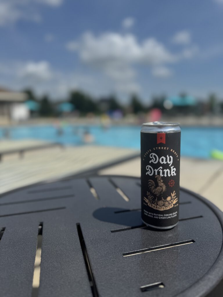Someone holding a Day Drink at the edge of a backyard pool.