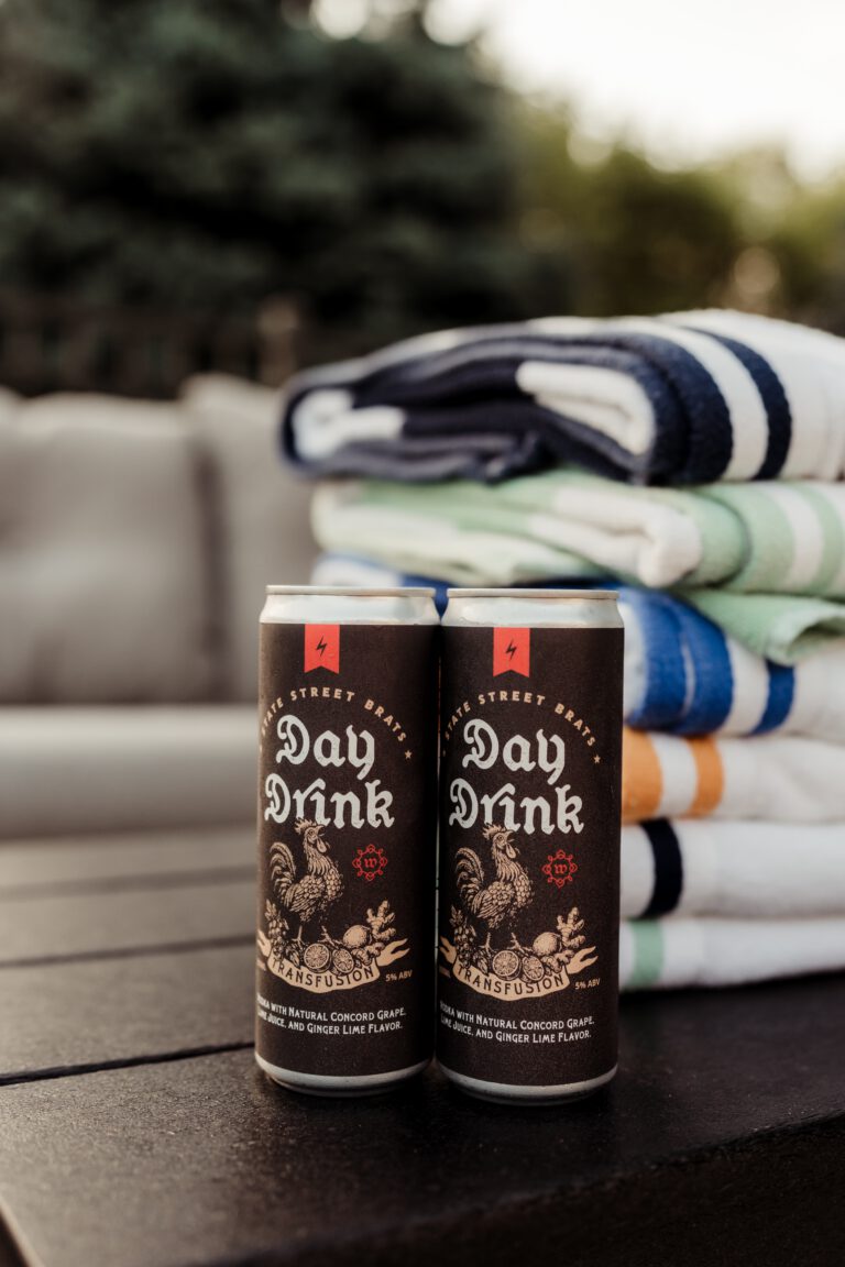 Two open cans of Day Drink on a beach towel in the sand.